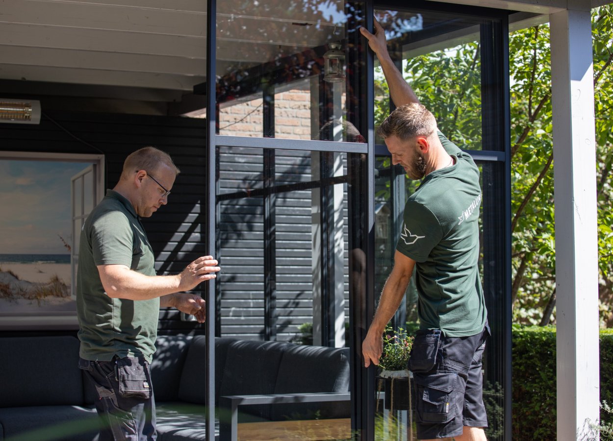 twee monteurs van metalura die een glazen wandsysteem aan het installeren zijn